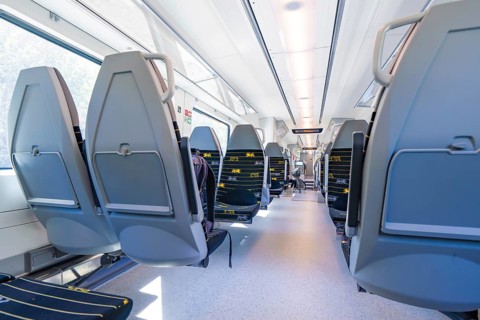 Modern train interior with rows of seats along large windows, battery Electric train with green