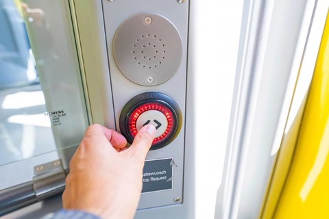 Hand operates a red illuminated stop button on a door in the vehicle, battery Electric train with
