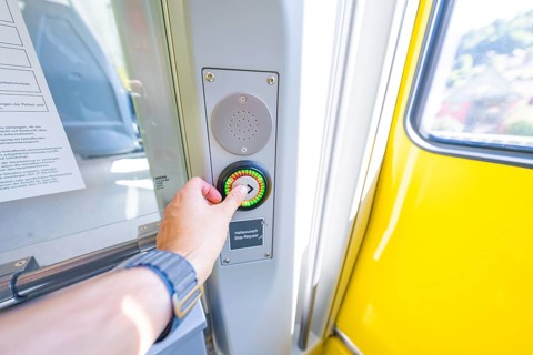 Hand presses stop button on a yellow door in the interior, battery Electric train with green