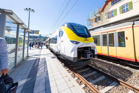 Modern yellow and white train at the station with green and red building in the background, battery