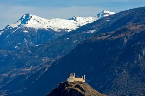 The ruins of Tourbillon Castle sit enthroned on a hill in front of the snow-capped mountains of the