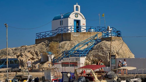 Small chapel on rocks with blue and white accents and blue roof, Chapel Agios Nikolaos, harbour,