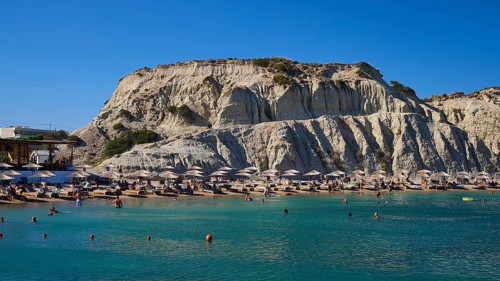 Lively beach against a rocky backdrop with bathing facilities and numerous parasols, Limanaki