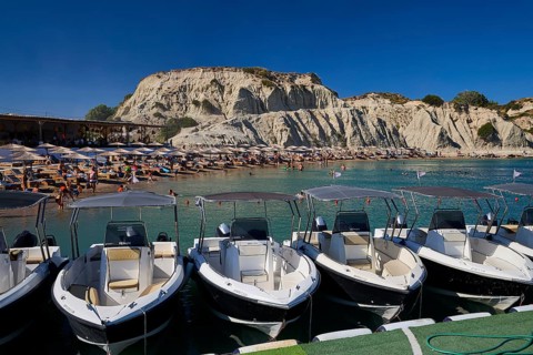 Boats in front of a rocky beach section with holiday atmosphere, many bathers and sunshades