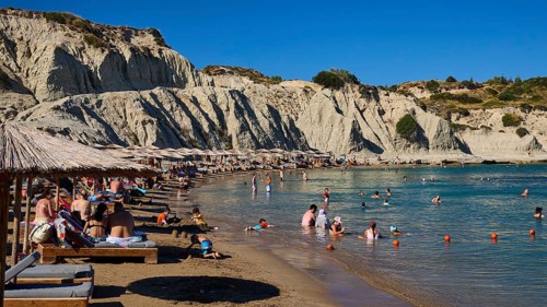 Pleasant scenery on the beach with beach loungers, bathers and magnificent rocky backdrop, Limanaki