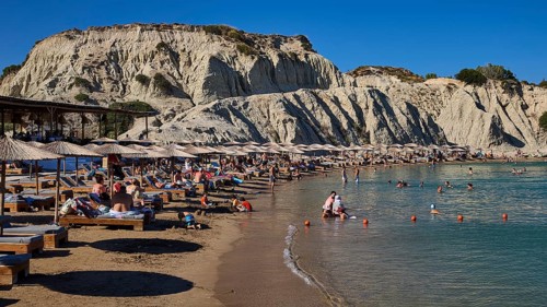 Long beach with sun loungers and bathers in front of an impressive rock face, Limanaki beach,
