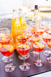 Several cocktail glasses with orange-coloured drink and orange slices, arranged on a table