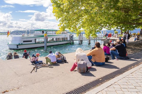 People sitting on the shore of a lake and watching an arriving ship, Lake Constance, Germany
