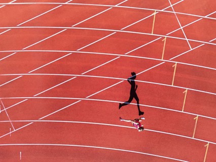 Aerial view of a female individual (runner) on a red athletics track (tartan track) with shadow as