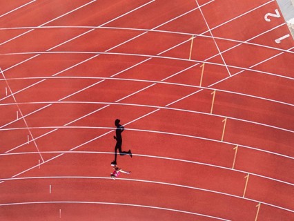 Aerial view of a female individual (runner) on a red athletics track (tartan track) with shadow as