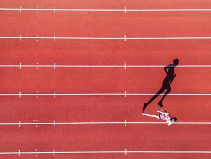 Aerial view of a female individual (runner) on a red athletics track (tartan track) with shadow as