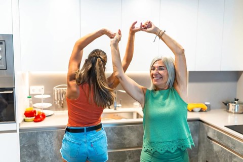 Two women joyfully dancing in a modern kitchen, embodying happiness and togetherness, surrounded by