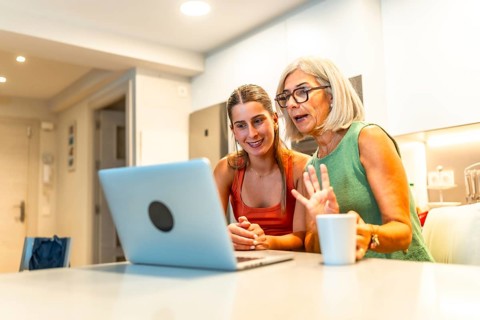 Senior and young women using laptop for a video conference with family, waving and smiling in