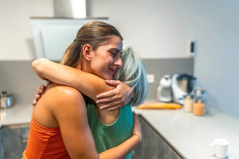Happy adult daughter is embracing her senior mother in a kitchen, showing love, care, and support