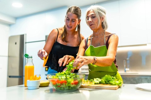 Mother and daughter preparing a mixed salad with lettuce, tomato, and orange juice in a modern