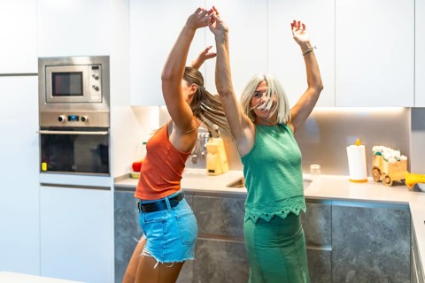 Two women enjoy a lively dance in a contemporary kitchen, celebrating happiness and friendship with