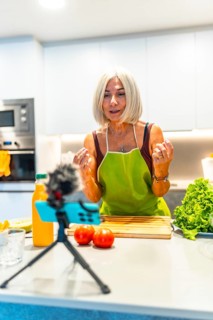 Cheerful mature food blogger engaging with her audience while recording a video tutorial on