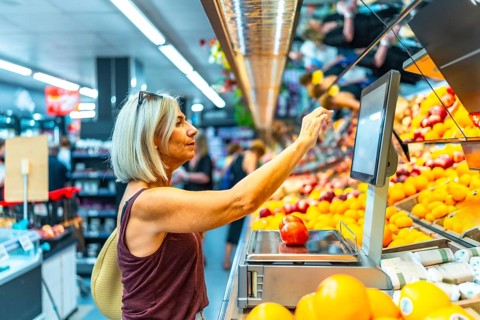 Senior woman using a digital weight scale to weigh fresh fruits at the supermarket, selecting her