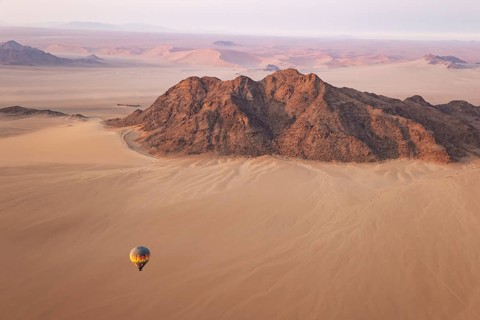 The hot-air balloon above an arid plain and isolated mountain ridges at the edge of the Namib