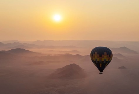 The hot-air balloon above an arid plain and isolated mountain ridges at the edge of the Namib