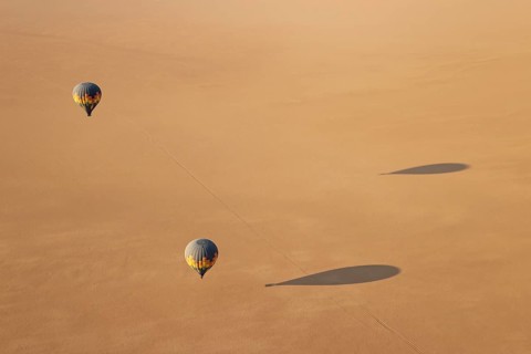 Two hot-air balloons above an arid plain at the edge of the Namib Desert. Aerial view from another