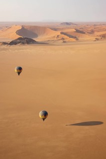 Two hot-air balloons above an arid plain at the edge of the Namib Desert. Aerial view from another
