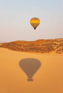 The hot-air balloon above an arid plain and isolated mountain ridges at the edge of the Namib