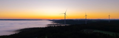 Row of wind turbines along the horizon at sunrise with fog in the distance, near Schorndorf,