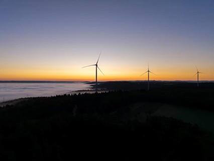 Three wind turbines in front of an orange and blue sky at sunrise with fog, near Schorndorf,