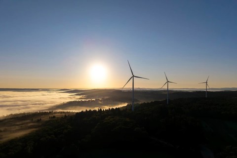Wind turbines rise into the sky above a misty forest at sunrise, near Schorndorf, Rems-Murr-Kreis,