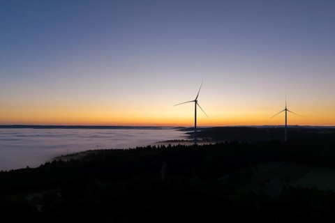 Two wind turbines in front of a colourful sunrise sky with fog over the landscape, near Schorndorf,