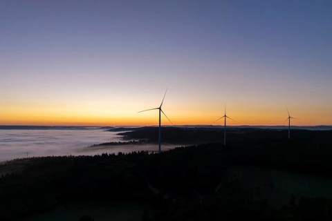 Wind turbines in front of a bright blue and orange sky at sunrise with fog over the landscape, near