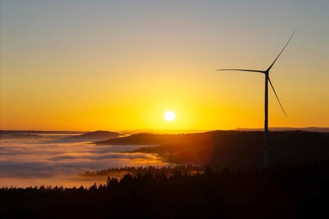 A wind turbine rises into the sunrise sky above misty hills, near Schorndorf, Rems-Murr district,