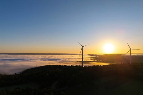 Two wind turbines rise above a fog-covered landscape in the morning light, near Schorndorf,