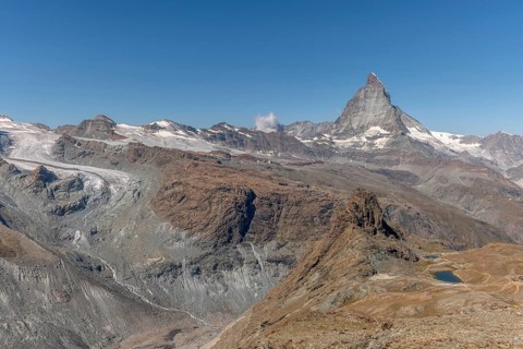 The towering peak of the Matterhorn dominates the clear sky, surrounded by rocky terrain and