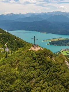 Group on a mountain with summit cross, overlooking a wide lake landscape, Herzogstand summit,