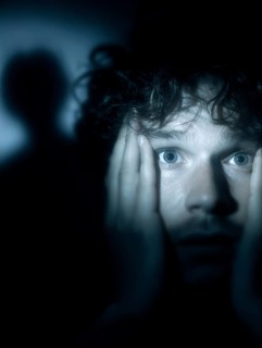An anxious man with wide open eyes staring into the darkness, shadow in the background, symbolic