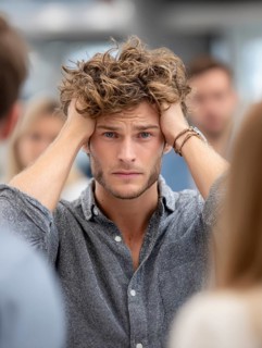 A young man with his hands to his ears, annoyed by an argument or noise in the background,