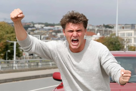 A man shouts angrily with clenched fists on a road, symbolic image for aggressive behaviour in road