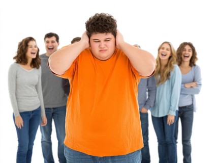 A sad boy in the foreground covers his ears while a group of teenagers laugh at him in the