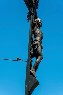 A detailed sculpture depicting Jesus on a cross rises against a bright blue sky. A small bird can