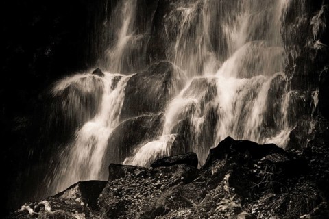 Vaucoux waterfall cascades gracefully over dark rocks, surrounded by lush greenery, Auvergne