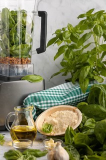 Blender with basil and sunflower seeds alongside other ingredients for pesto