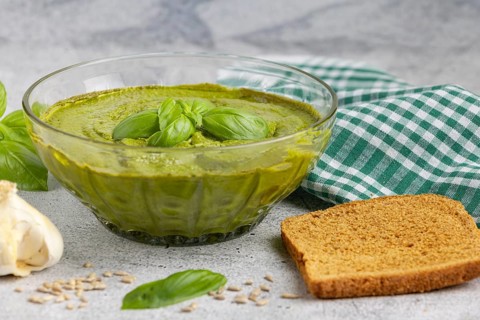 Basil pesto in a glass bowl with bread, garlic and chequered cloth
