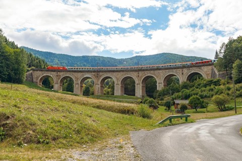 Train crossing Adlitzgraben viaduct, cloudy sky and green hills, Semmering railway, Semmering,