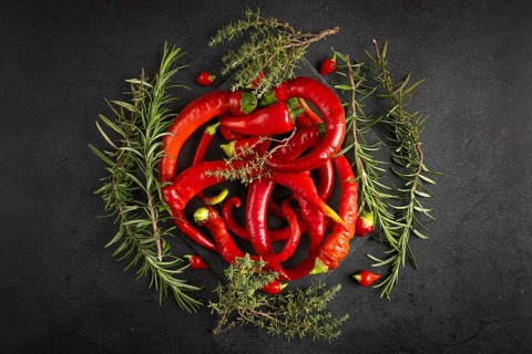 Red peppers, chilli peppers and herbs arranged on a dark background