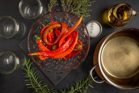 Hot peppers with empty jars, herbs and cooking pot on a dark table