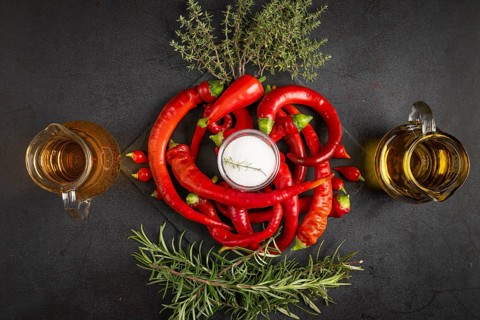 Hot red peppers with vinegar, oil, salt and herbs on a black background