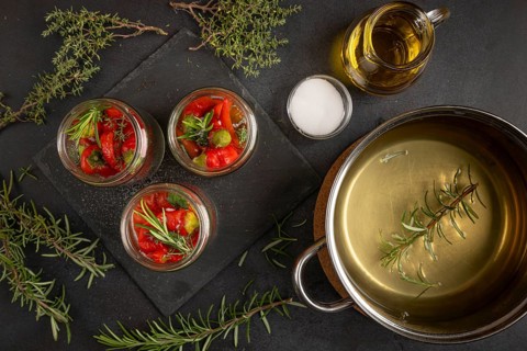Cooking pot, herbs and jars filled with hot peppers on a dark background