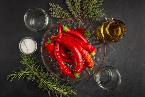 Several red peppers, chilli peppers alongside oil, salt, herbs and empty jars